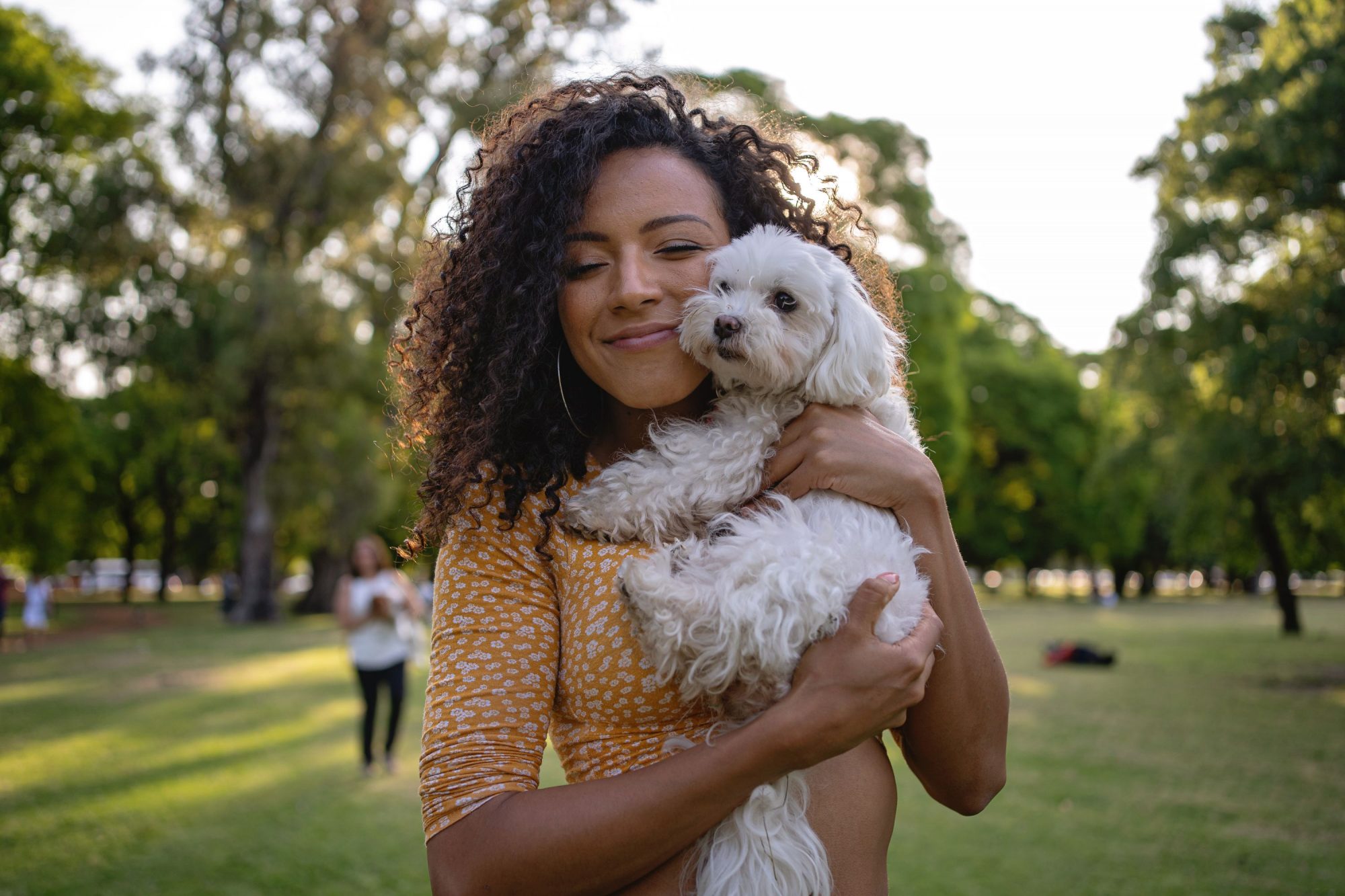 A woman holds her small, white dog in a park.